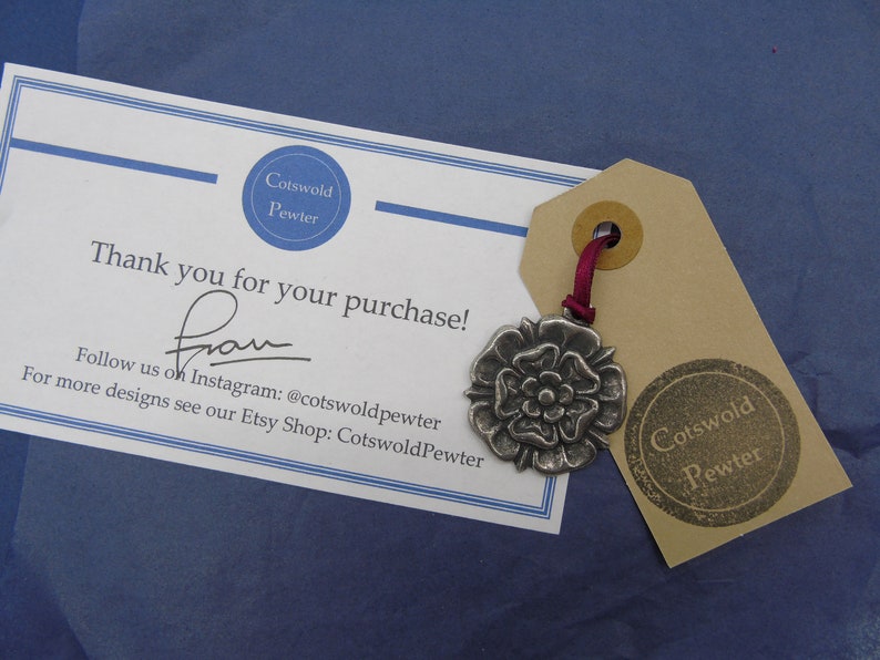 May include: A thank you card from Cotswold Pewter with a silver charm of a white rose on a brown tag. The card says "Thank you for your purchase!" and includes contact information for the shop on Instagram and Etsy.