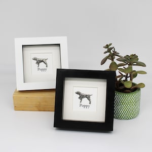 May include: Two framed pictures of a dog, one with a white frame and one with a black frame. Both pictures have the name "Poppy" written below the dog.