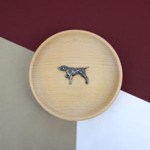 May include: A silver-coloured metal figurine of a dog standing on a light brown wooden plate.