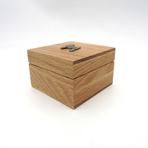 May include: A small wooden box with a hinged lid. The box is made of light brown wood and has a small metal dog figurine on the top.