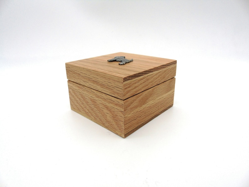 May include: A small wooden box with a hinged lid. The box is made of light brown wood and has a small metal dog figurine on the top.