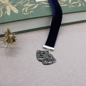May include: A blue velvet bookmark with a silver charm of two theatre masks, one smiling and one frowning.