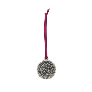 May include: A silver metal ornament shaped like a rose with a red ribbon attached.