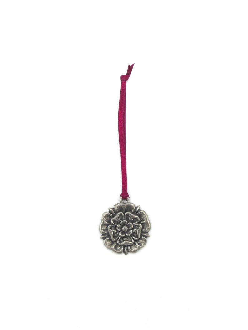 May include: A silver metal ornament shaped like a rose with a red ribbon attached.
