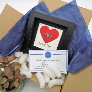 May include: A small framed print with a red heart and a silver Celtic knot. The text "Gr&aacute; go Deo" is written below the heart. The print is packaged in a cardboard box with blue tissue paper and white packing peanuts.