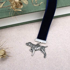 May include: A blue velvet bookmark with a silver metal dog charm. The dog is in a standing position with its head turned to the side.