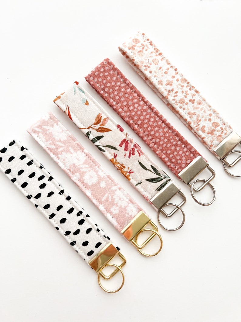 May include: Five keychains with different fabric patterns and gold and silver key rings. The patterns include floral, polka dots, and abstract black and white.