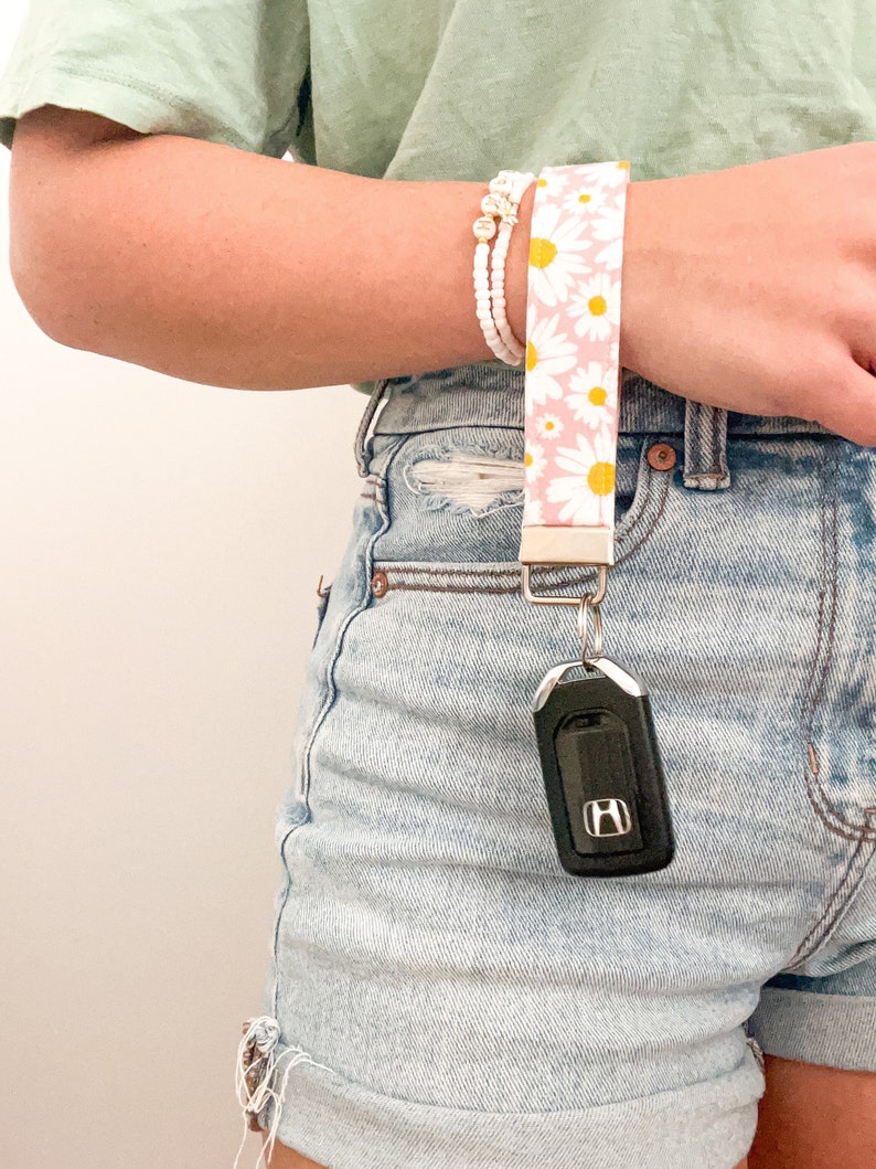 May include: A pink and white daisy patterned key chain with a silver key ring and a black car key with a silver Honda logo.