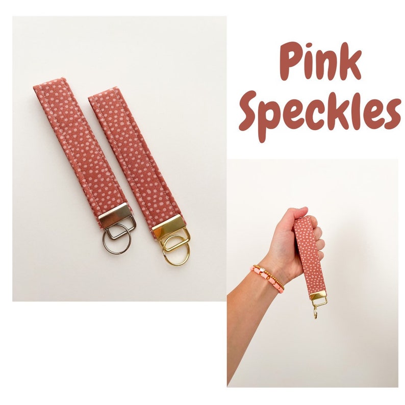 May include: Two pink keychains with white polka dots and gold key rings. The keychains are made of fabric and have a simple design. The text "Pink Speckles" is visible in the image.