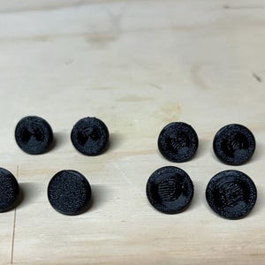 Pode incluir: Oito botões redondos pretos com uma superfície texturizada e um design em relevo.