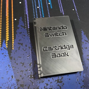 May include: A grey 3D printed Nintendo Switch Cartridge Book. The book has a spine and is designed to hold game cartridges.
