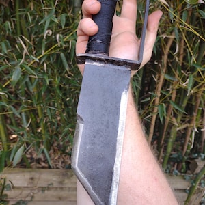 May include: A black metal knife with a long, pointed blade and a wrapped handle. The knife is held in a hand.