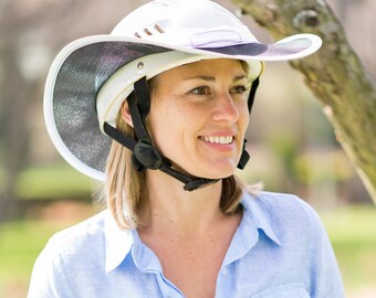 Pode incluir: Um capacete branco com uma viseira de sol de aba larga. O capacete tem uma correia preta e uma fivela preta. A pessoa que usa o capacete está sorrindo e olhando para a direita.