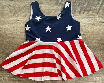 May include: A red, white, and blue sleeveless dress with a ruffled skirt. The top of the dress is a solid blue with white stars, and the skirt is striped with red and white.