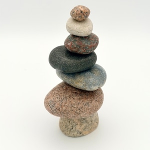 May include: A set of three ceramic mugs with a speckled, matte finish. The mugs are in shades of cream, light gray, and dark gray. Each mug has a simple, minimalist design and a rounded handle.