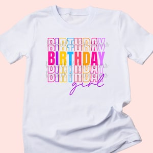 Peut inclure: T-shirt blanc avec le texte "BIRTHDAY girl" en couleurs arc-en-ciel. Le mot "birthday" est empilé plusieurs fois sur lui-même.