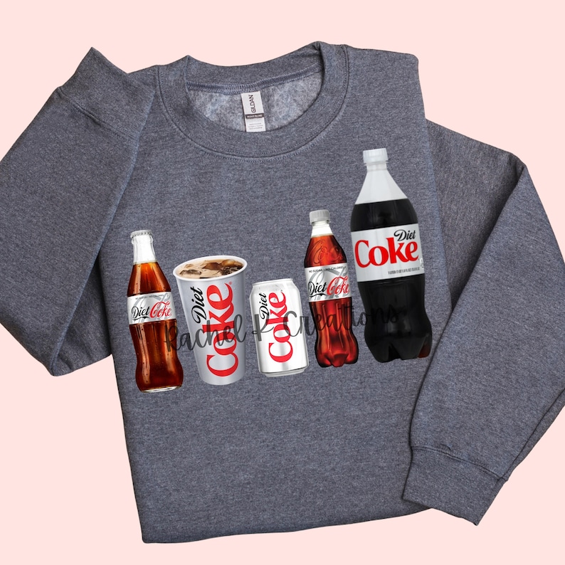 May include: A gray sweatshirt featuring a graphic of Diet Coke bottles, cans, and a cup. The Diet Coke logo is prominently displayed on each item. The sweatshirt has a crew neck and long sleeves. The brand name "Gildan" is visible on the tag.