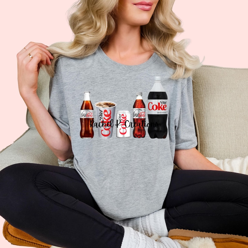 May include: A gray t-shirt featuring a graphic of Diet Coke products: a glass bottle, a cup, a can, and a plastic bottle. The text "Diet Coke" is visible on the products. The text "Rachel P Creations" is also visible.