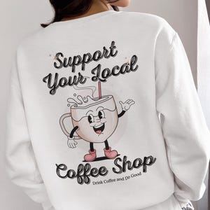 May include: White sweatshirt with a graphic of a cartoon coffee cup with the text "Support Your Local Coffee Shop" and the tagline "Drink Coffee and Do Good".