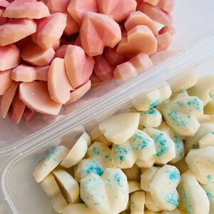 May include: Two containers filled with heart-shaped wax melts. One container has pink wax melts, the other has white wax melts with blue glitter.