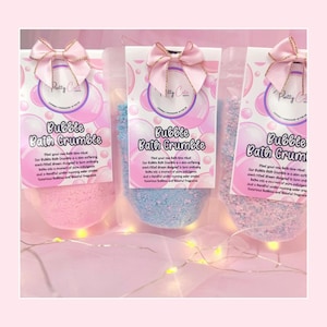 May include: Three clear bags of bubble bath crumbles in pink, blue, and lavender. Each bag has a pink bow and a label with the text "Patty C" and "Bubble Bath Crumble". The bags are filled with colorful granules.