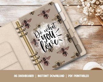May include: A beige planner with gold rings and a removable cover featuring a beige background with a watercolour effect and the text "Do what you love" in black script. The cover is decorated with a repeating pattern of brown and black bees.