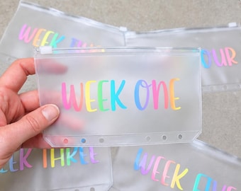 May include: A set of translucent, frosted plastic zipper pouches for binders, each featuring colorful, gradient-style text. The pouches are labeled with sequential weeks, including Week One, Week Three, Week Four, and Week Five, printed in a vibrant rainbow font.