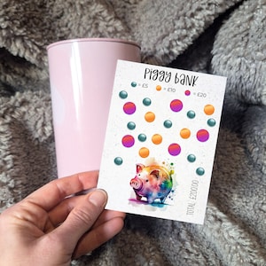 May include: A colourful piggy bank chart with a watercolour piggy bank illustration. The chart has circles in green, orange, and purple, representing different amounts of money. The text on the chart reads "Piggy bank", "£5", "£10", "£20", and "TOTAL: £200.00".