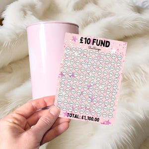 May include: A pink and white card with a pink glitter background and white stars. The card says "£10 FUND Challenge" and has a grid of 100 circles with "£10" written in each circle. The total amount is "£1,100.00".