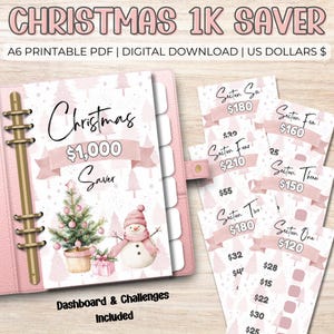 May include: A pink Christmas savings planner with a binder, featuring a Christmas tree and snowman illustration. Includes challenge cards for saving £1,000. The cover reads "Christmas £1,000 Saver".