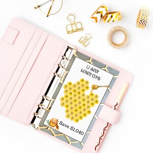 May include: A pink planner with a 57 week honey comb savings chart. The chart is a honeycomb design with the number 10 in each cell. The chart is labeled "57 week honey comb" and "Save $1,040".