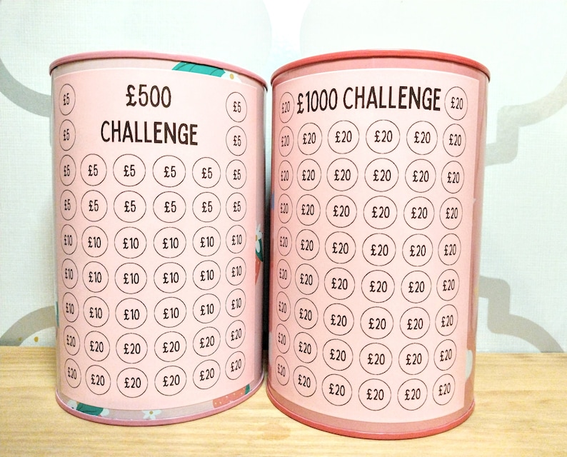 Może przedstawiać: Dwie cylindryczne metalowe puszki na pieniądze z r&oacute;żowymi etykietami. Lewa puszka ma napis &pound;500 CHALLENGE z rzędami k&oacute;łek oznaczonych &pound;5, &pound;10 i &pound;20. Prawa puszka ma napis &pound;1000 CHALLENGE z rzędami k&oacute;łek oznaczonych &pound;20.