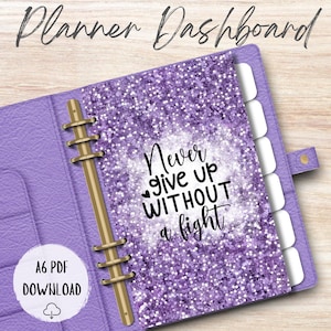 May include: A purple planner dashboard with a glittery design and the text "Never give up without a fight." The planner has a gold binder and white tab dividers. The text "A6 PDF DOWNLOAD" is also visible.