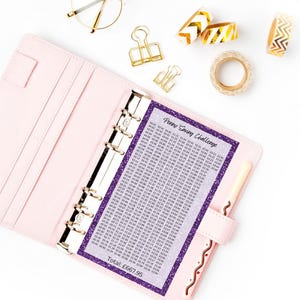 May include: A light pink six-ring binder containing a purple glitter-bordered Penny Saving Challenge tracker sheet with a grid of monetary values and the text Total: &pound;667.95. The binder is accompanied by gold binder clips and gold patterned tape.