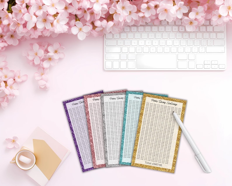 May include: Five rectangular Penny Saving Challenge trackers with glittery borders in purple, pink, silver, teal, and gold. Each tracker features a grid of numbers and the text Penny Saving Challenge. A white pen rests on the gold tracker.