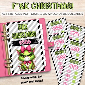 May include: A pink binder with a green Grinch-like cat graphic and the text "F*&K CHRISTMAS!" and "$500". Includes savings tracker sheets with amounts from $5 to $150. The text "Saving money has never been easier!" is also present.