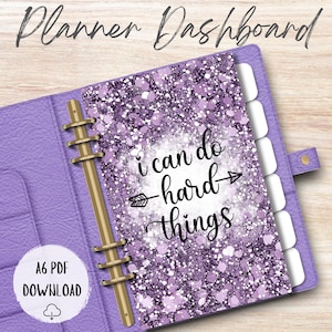May include: A purple planner dashboard with the text "Planner Dashboard" at the top. The insert has a glittery purple design with the words "I can do hard things" in black script. The planner has gold rings and a button closure.