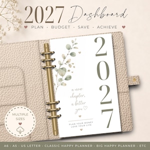 May include: A 2027 dashboard planner insert featuring a vertical eucalyptus branch illustration, the text 2027, a new chapter, a better you, and plan your money love your life. The page is held in a beige textured binder with gold rings.