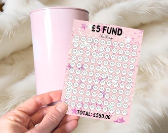 May include: A light pink tumbler next to a rectangular savings tracker card featuring a pink background with white stars and circles labeled £5. The text reads £5 FUND Challenge and TOTAL: £550.00 in bold black lettering on the card.