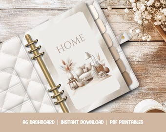 May include: A white A6 dashboard planner with a quilted cover. The planner is open, revealing a page with the word "HOME" and an illustration of a living room. The planner has gold-colored rings and tabs. The bottom of the image has text that reads "A6 DASHBOARD | INSTANT DOWNLOAD | PDF PRINTABLES."