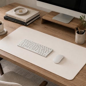 May include: A large, rectangular, off-white desk mat with rounded corners, positioned on a wooden desk surface. The mat serves as a base for a white wireless keyboard and a white computer mouse, providing a clean, smooth workspace area.