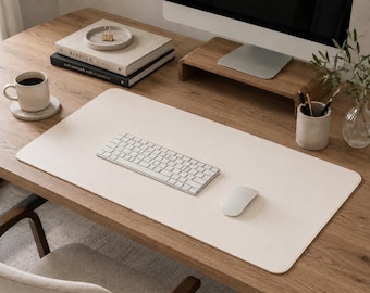 Könnte beinhalten: Eine große, rechteckige, cremeweiße Schreibtischunterlage mit abgerundeten Ecken auf einem Schreibtisch aus Holz. Die Unterlage dient als Basis für eine weiße kabellose Tastatur und eine weiße Computermaus für einen sauberen Arbeitsbereich.