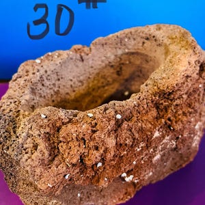 May include: A rough-textured, brown, and reddish-brown stone bowl. The number "30" and a hashtag symbol are written in black marker on the blue background. The bowl has a rounded shape with a hollowed-out interior.