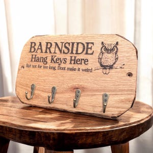 以下が含まれることがあります： フクロウのイラストと「BARNSIDE Hang Keys Here But not for too long. Dont make it weird.」という文字が刻印された、自然な縁を持つ長方形の木製キーホルダー。アンティーク調の真鍮色をした金属製フックが4つ付いています。