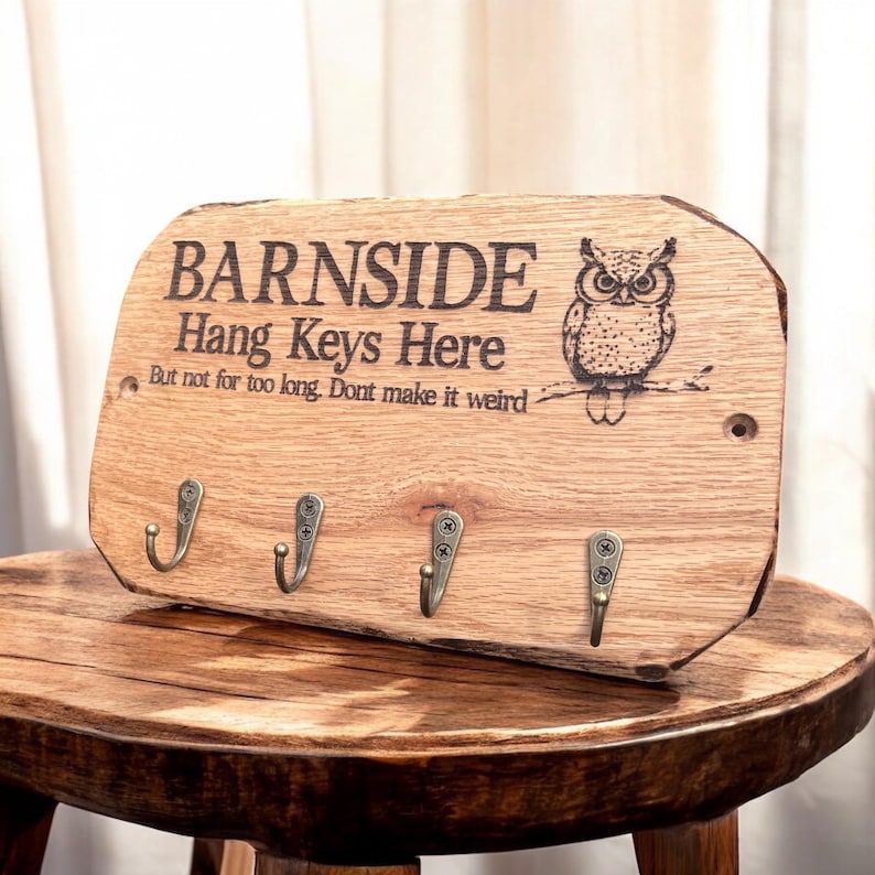 以下が含まれることがあります： フクロウのイラストと「BARNSIDE Hang Keys Here But not for too long. Dont make it weird.」という文字が刻印された、自然な縁を持つ長方形の木製キーホルダー。アンティーク調の真鍮色をした金属製フックが4つ付いています。
