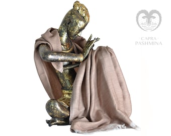 May include: A brown pashmina shawl draped over a golden statue. The shawl has a subtle texture and a fringed edge. The statue is of a person in a seated pose, with their head bowed and hands clasped together. The background is white.