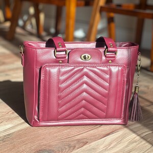 May include: A burgundy quilted tote bag with a gold zipper and a gold tassel. The bag has a front pocket with a gold clasp.