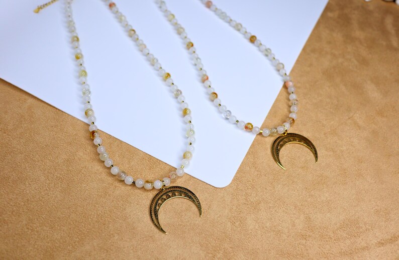 May include: Two delicate necklaces with gold crescent moon pendants. Each necklace features small white and light brown beads.