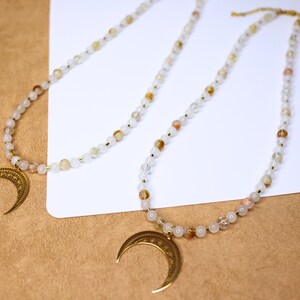 May include: Two gold crescent moon pendants on necklaces with white and light brown beads.