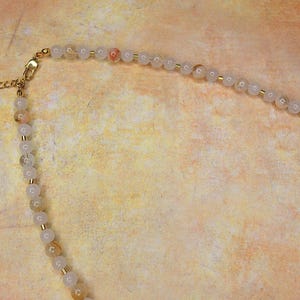 May include: A gold chain necklace with a clasp and a strand of white and light pink beads.